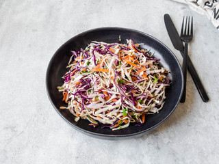Red cabbage, carrot, cabbage coleslaw salad on black plate on grey background.