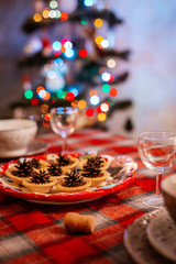 Traditionally decorated Christmas table. Creative decoration of the festive table cones on a plate on the background of bokeh lights.