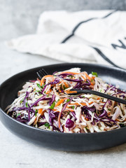 Red cabbage, carrot, cabbage coleslaw salad on black plate on grey background. Copy sapce