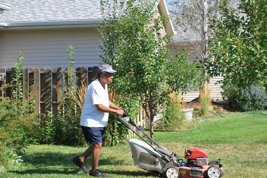 African American Male Mowing The Lawn Outside.