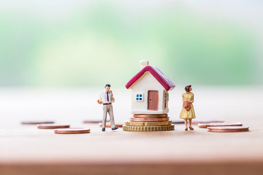 selective focus of miniature angry woman with miniature man and mini house on stack coins over blurred green garden background  for Asset management after divorce concept.