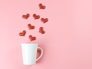 Flat layout image of of red glitter hearts splash out from white coffee cup on pink background