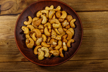 Ceramic plate with roasted cashew nuts on a wooden table. Top view