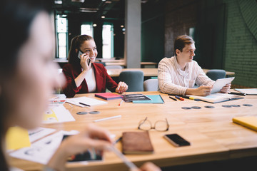 Cheerful adult female worker talking on mobile in meeting room
