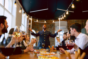 Happy co-workers celebrating while company party, corporate event. Young caucasian people in business attire talking, drinking wine. Concept of office culture, teamwork, friendship, holidays, weekend.
