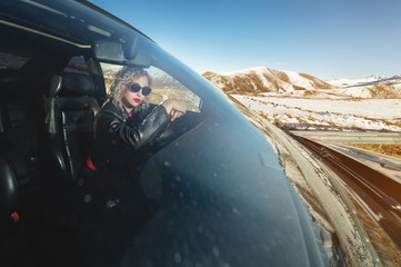 Attractive Caucasian girl in sunglasses and a leather jacket sits at the wheel of a sports retro car with a leather interior. Woman driving concept