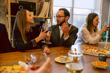 Happy co-workers celebrating while company party, corporate event. Young caucasian people in business attire talking, drinking wine. Concept of office culture, teamwork, friendship, holidays, weekend.