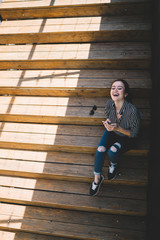 Young excited woman using smartphone on stairs in sunny day