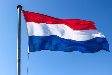 Dutch flag on a flagpole waving in the wind, close up, on a clear blue sky day isolated