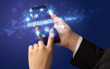 Female hand holding smartphone with BIOTECHNOLOGY inscription, modern technology concept
