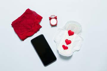 Female lace red panties with medical female slim cotton menstruation pad, phone and love shape on a blue background. Menstruation