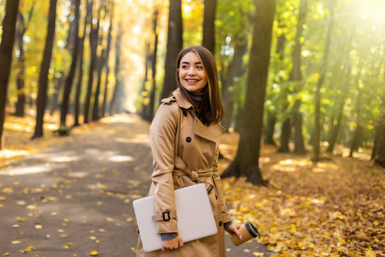 Young pretty woman walking laptop and coffee in autumn park.