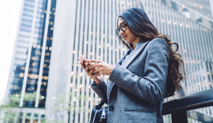 Young ethnic female in blazer messaging on phone on urban background