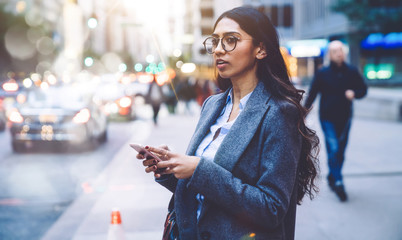 Obraz premium Ethnic female standing on sidewalk with smartphone