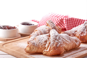 Still life with sugared croissants, fruit jam and red dish on wooden table top.