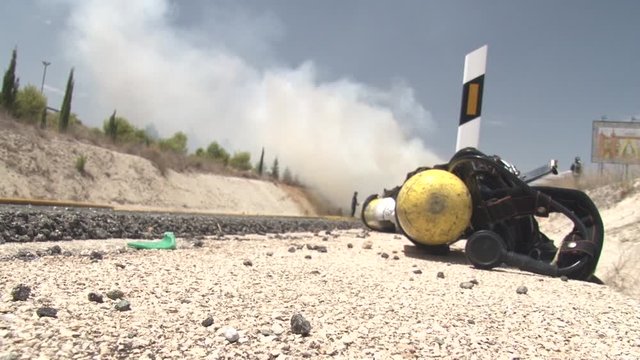 Drastic car crash site with smoke emissions on terrian with firefighters extinguishing