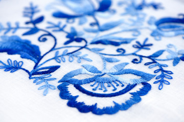 Hand embroidery stitch on a thin canvas. Blue floral ornament on a white background. Art and craft conception.