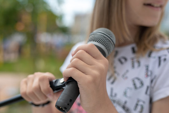 Young girl holding mic with two hands. Microphone and girl singer close up. Cropped image of female teen singer in park.