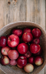 Delicious freshly harvested organic autumn red apples inside a wicker basket, stand-in on the wooden table, close up view