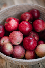 Delicious freshly harvested organic autumn red apples inside a wicker basket, stand-in on the wooden table, close up view