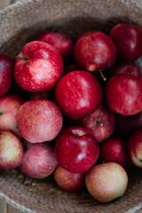 Delicious freshly harvested organic autumn red apples inside a wicker basket, stand-in on the wooden table, close up view