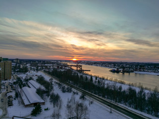 Red-orange sunset over a wide river in a band of light clouds over a snow-covered city