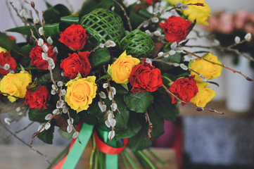 Close up photo of bouquet of yellowroses, red roses and willow branches with fluffy catkins wrapped with red and green ribbon