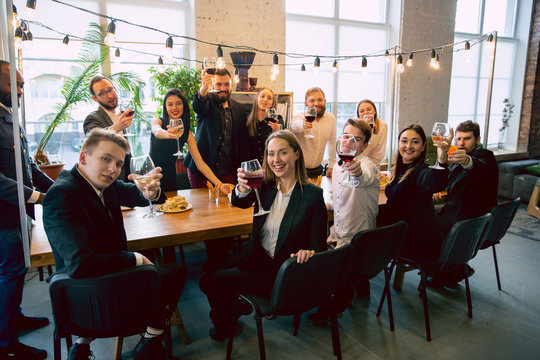 Happy co-workers celebrating while company party and corporate event. Young caucasian people in business attire cheering, laughting. Concept of office culture, teamwork, friendship, holidays, weekend.
