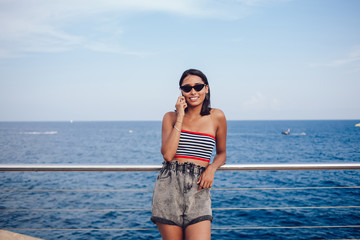 Half length portrait of smiling millennial woman using roaming internet connection for communicate with travel colleague while resting with promenade time, happy hipster girl in sunglasses phoning