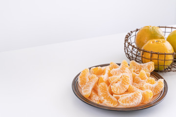 Beautiful peeled tangerines in a plate and metal basket isolated on bright white clean table in a modern contemporary kitchen island, close up.