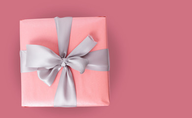 Single pink gift box with silver ribbon on red background.