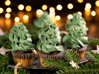 Green christmas cupcake with stsprinkles on wooden background with garland lights bokeh, copy space. Close up. Christmas and new year holidays background concept.
