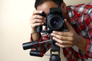 Adult man holding an old and vintage medium format film camera on a tripod.