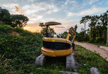 The modern excavator on the construction site with sunset sky. Large tracked excavator standing on a hill with a green grass. Machinery for a construction of a new building in the countryside. © Volodymyr_sh