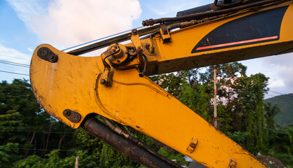 Details of modern excavator on the construction site with sunset sky. Large tracked excavator standing on a hill with a green grass. Machinery for a construction of a new building in the countryside.