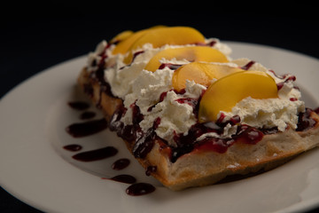 waffle topped with whipped cream, sauce and fruit