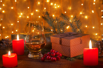 Glass with cognac or whiskey, Christmas balls and candles on blur lighting background. New Year's tree, balls and glass with alcohol. Happy holidays decoration.