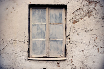 Old white painted window on aged white wall with cracks