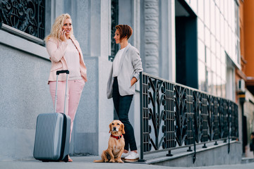 Two business woman standing on the street with suitcase and calling taxi