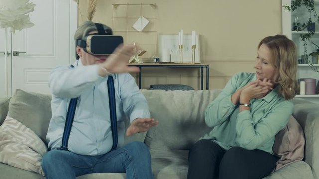 Aged woman is watching her husband using VR-glasses