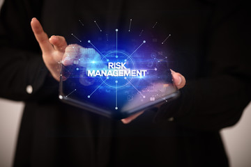 Businessman holding a foldable smartphone with RISK MANAGEMENT inscription, new business concept