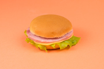 Sandwich with ham, cheese, lettuce on orange background.