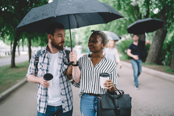 Multiracial couple walking beneath umbrella in city