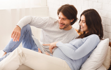 Obraz premium Pregnant woman and her husband using digital tablet in bed