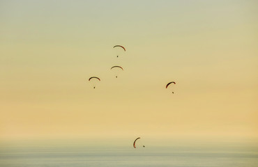 Silhouette of powered paraglider soaring flight over the sea against marvellous orange sunset sky.