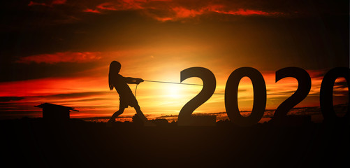 Silhouette of girl tugging on a rope number 2020 in sunset background. Happy new year holiday concept.
