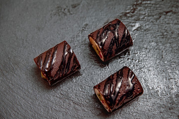 Photo of Chocolate Maki Sushi Pancake Rolls Stuffed with Fruits and Cheese Top View. Sliced Dessert with fruits and Sweet Brown Sauce on a black slate board