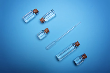 Liquid or oil in small bottles with cork plugs and dropper on light blue background. Top view. Flat lay.