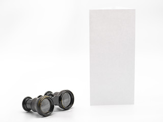 Antique opera glasses isolated on white background with mockup white vertical leaflet mockup paper with free space for text. Black small vintage binocular and theatre programme mock up.