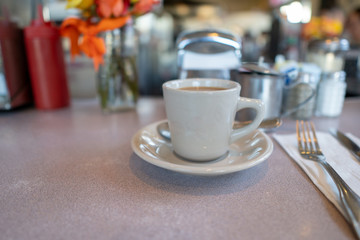 Classic American diner scene with white coffee cup, silverware, and napkin on speckled table